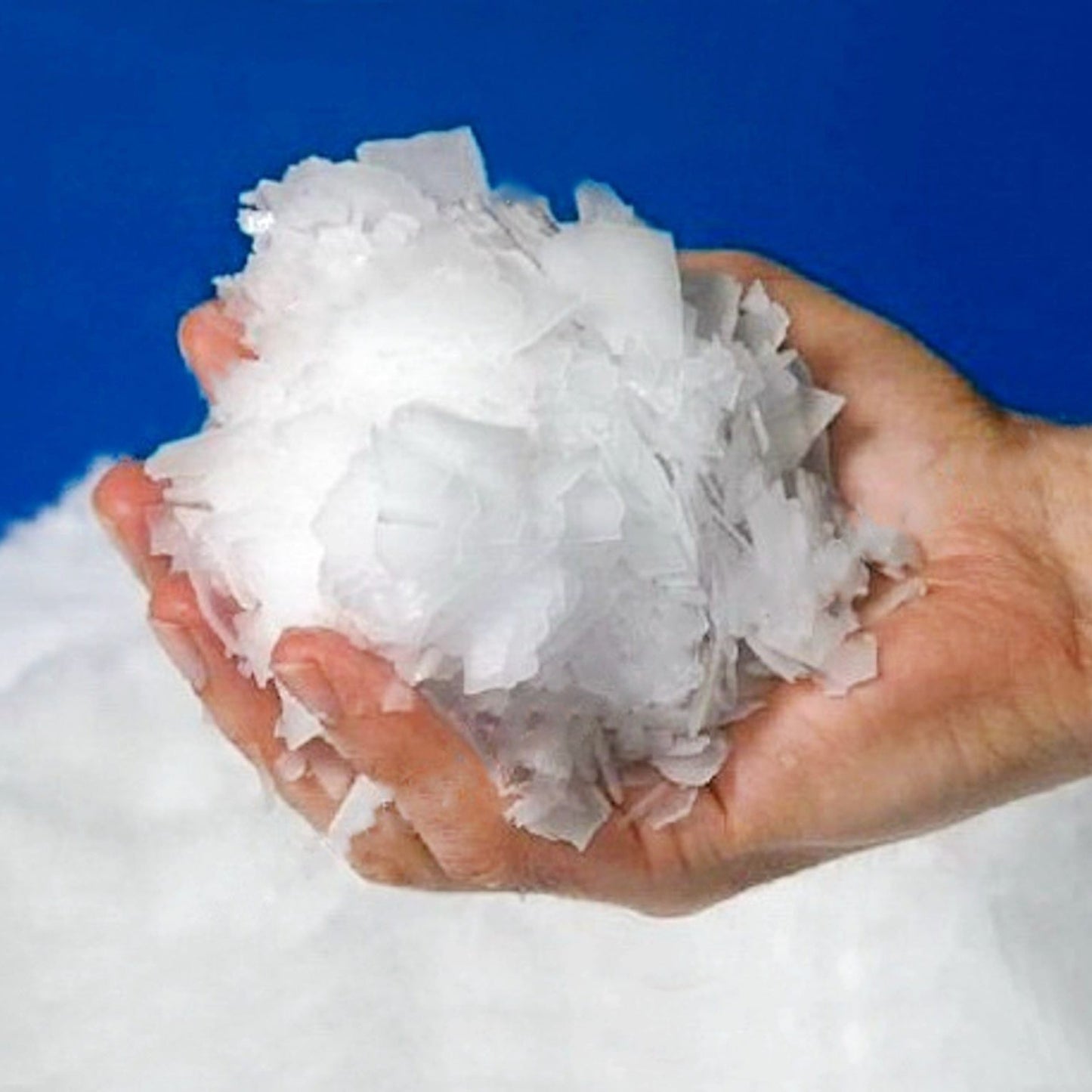 Person holding a handful of Flake Ice in front of a blue background.